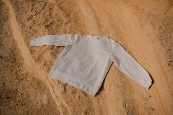 Plain white crew neck sweatshirt mockup lying flat on a sandy texture, perfect for apparel design presentation.
